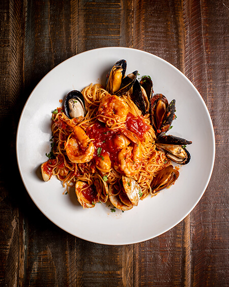 A beautifully presented plate of Angel Hair Pescatore on a wooden counter — $19.95