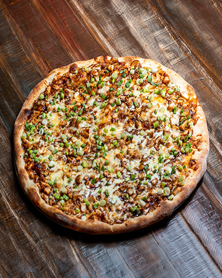 A beautifully presented BBQ Chicken Bacon Cheddar pizza pie on a wooden counter — $19.80