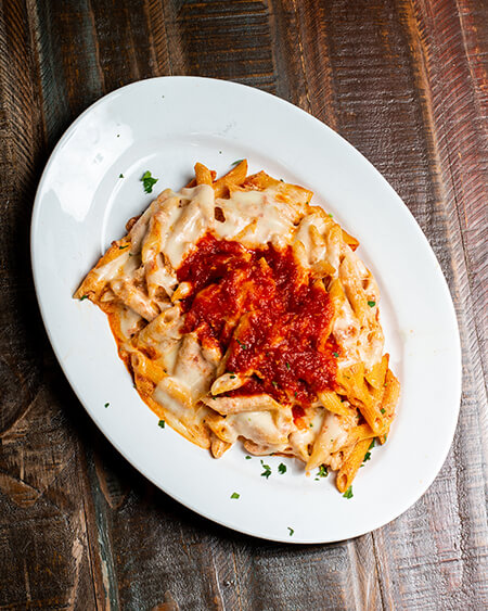 Baked Ziti with fresh basil plated on a round white dish and placed on a wooden table