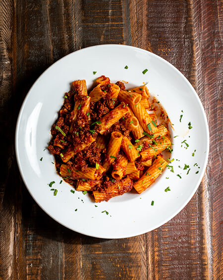 A beautifully presented plate of Bolognese Meat Sauce pasta on a wooden counter — $11.75