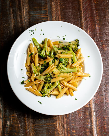 A beautifully presented plate of Broccoli, Garlic and Oil Sauce pasta on a wooden counter — $9.50