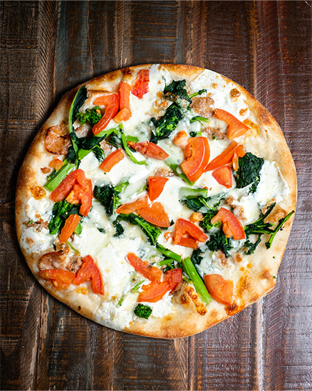 A beautifully presented Broccoli Rabe Combo pizza pie on a wooden counter — $22.00