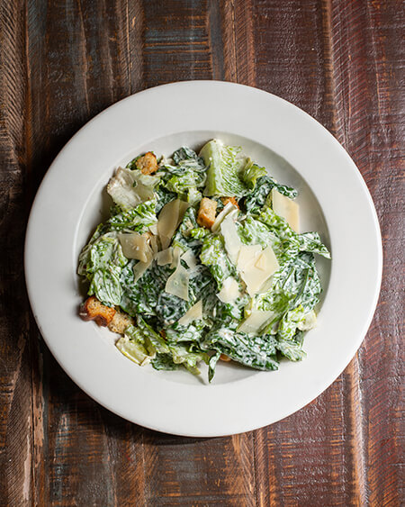 A beautifully presented plate of Caesar Salad on a wooden counter — $6.95