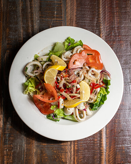 A beautifully presented plate of Calamari Salad on a wooden counter — $13.50