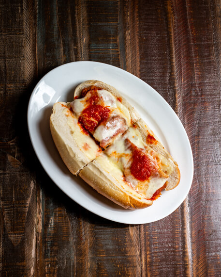 A beautifully presented Chicken Breast Parmigiana Hot Sandwich on a wooden counter — $8.50