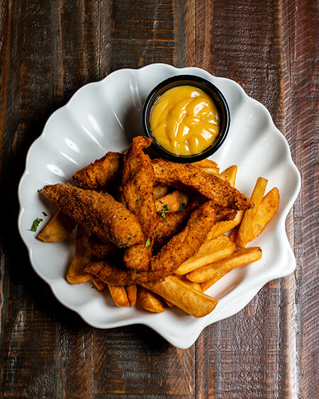 A beautifully presented plate of Chicken Fingers and Fries on a wooden counter — $10.95