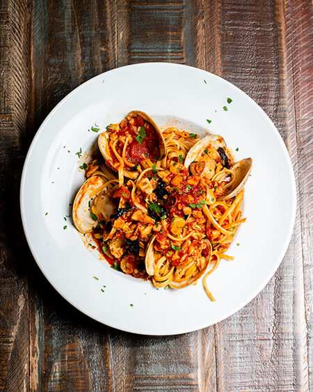 A beautifully presented plate of Red Clam Sauce pasta on a wooden counter — $15.95