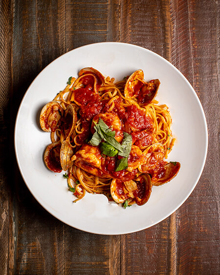 A beautifully presented plate of Clams and Shrimp Fra Diavolo pasta on a wooden counter — $18.95