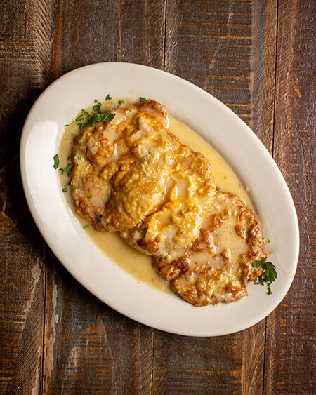 A beautifully presented plate of Francese Veal on a wooden counter — $16.95