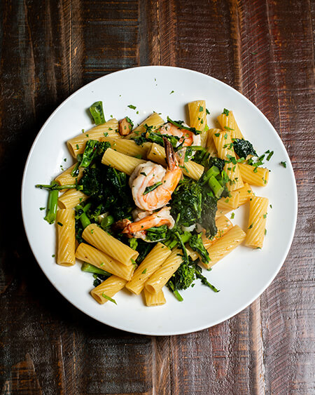 Rigatoni and Shrimp Pasta with Broccoli Rabe Garlic and Oil plated in a white bowl laid on a wooden table