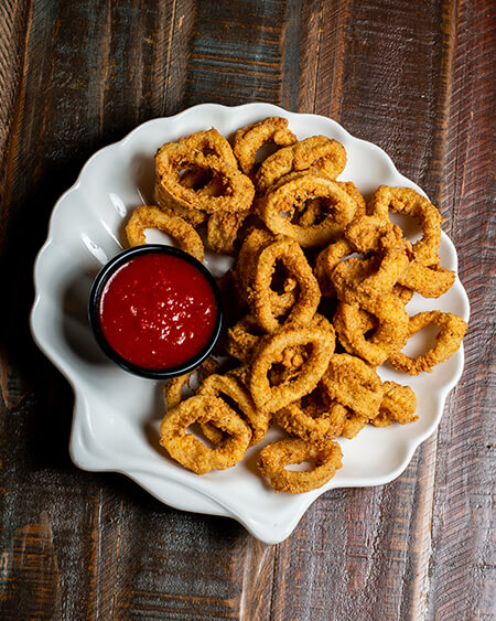 A beautifully presented plate of Fried Calamari Toscana on a wooden counter — $10.95