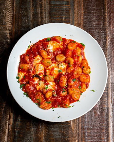 A beautifully presented plate of Gnocchi Sorrentina on a wooden counter — $14.95