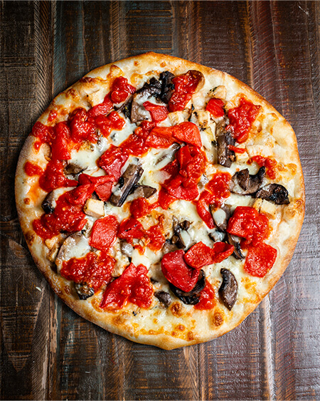 A beautifully presented Grilled Chicken Portobello and Roasted Pepper Pizza pie on a wooden counter — $19.80