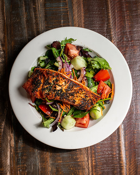 Herb Crusted Salmon over a mixed green salad placed in a white dish on a wooden table.