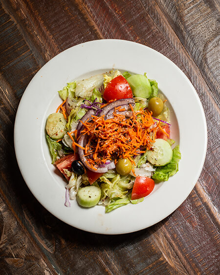 House Salad with house dressing on a white round dish placed on a wooden table