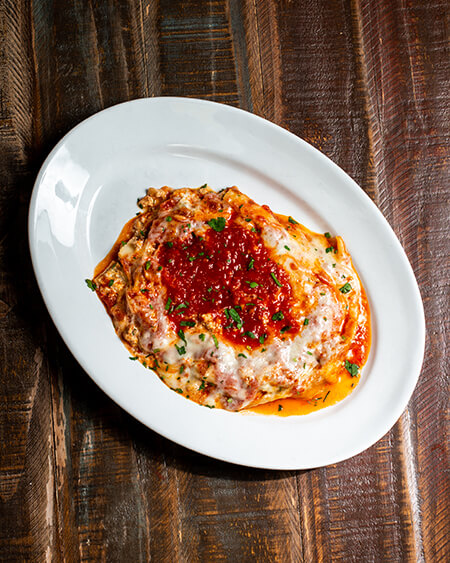 A beautifully presented plate of Lasagna on a wooden counter — $11.50