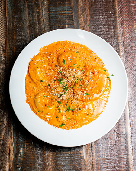 A beautifully presented plate of Lobster Ravioli on a wooden counter — $18.95