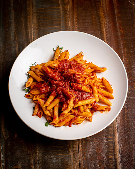 A beautifully presented plate of Marinara Sauce pasta on a wooden counter — $9.50