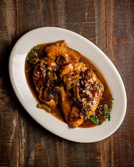A beautifully presented plate of Chicken Marsala on a wooden counter — $13.50