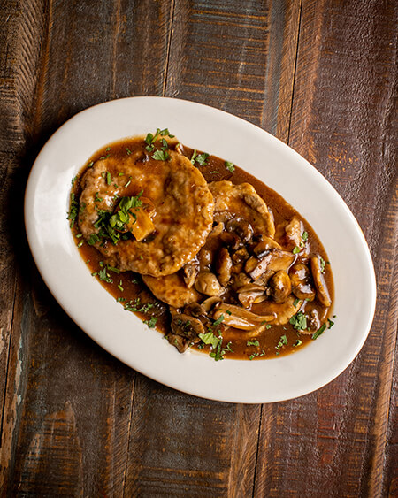 A beautifully presented plate of Veal on a wooden counter — $16.95