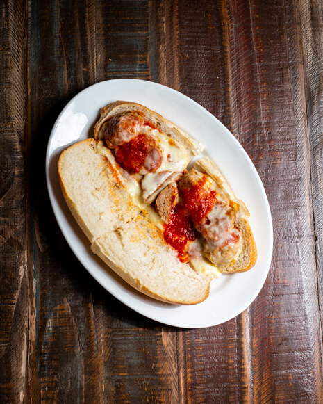 A beautifully presented Meatball Parmigiana Hot Sandwich on a wooden counter — $8.50