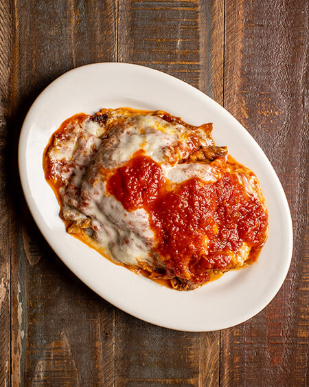 A beautifully presented plate of eggplant parmigiana or rollatine on a wooden counter — $15.95