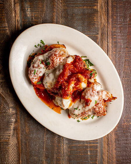A beautifully presented plate of Parmigiana Shrimp on a wooden counter — $18.95