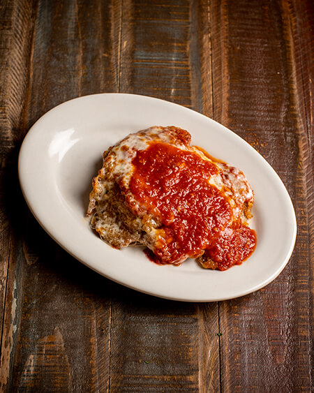 A beautifully presented plate of Parmigiana Veal on a wooden counter — $16.95