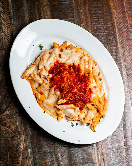 A beautifully presented plate of Pasta al Forno on a wooden counter — $12.95