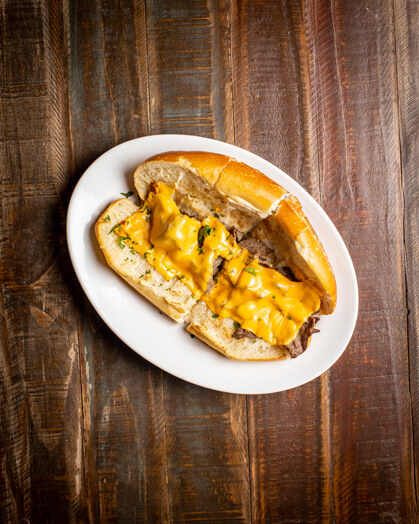 A beautifully presented Steak and Cheese Hot Sandwich on a wooden counter — $10.00