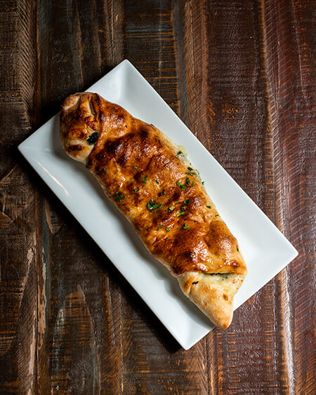 A beautifully presented plate of Stromboli on a wooden counter — $8.95