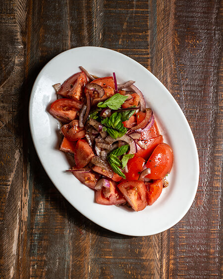 Tomato and red onion salad plated on a round white dish on a wooden table.