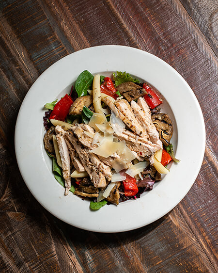 A beautifully presented plate of Tuscan Chicken on a wooden counter — $13.95