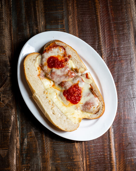 A beautifully presented Veal Cutlet Parmigiana Hot Sandwich on a wooden counter — $10.50