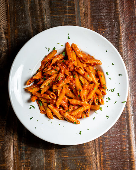 A beautifully presented plate of Penne Vodka on a wooden counter — $12.95