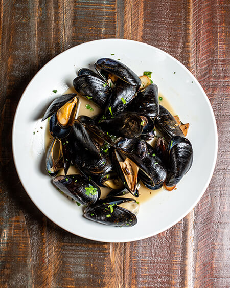 A beautifully presented plate of Zuppa di Mussels on a wooden counter — $11.95